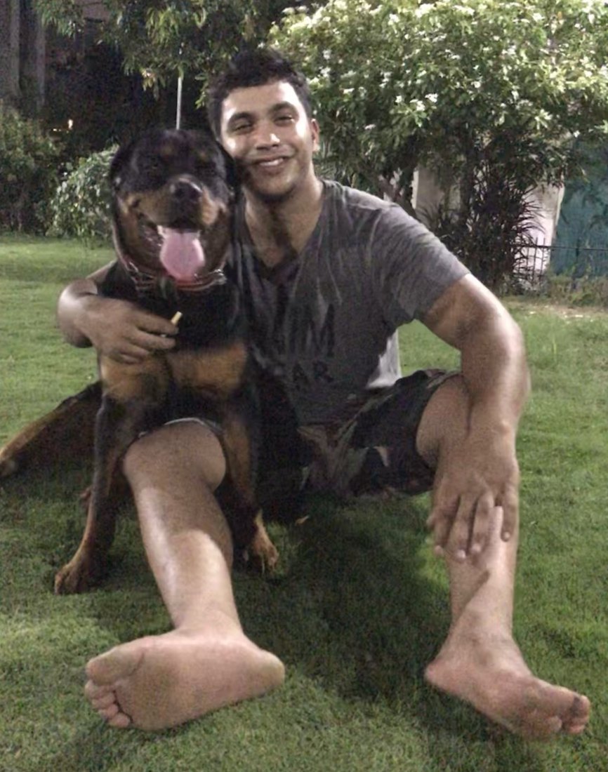 Soutik sitting on the grass in the evening with his arm round Luna, a Rottweiler
